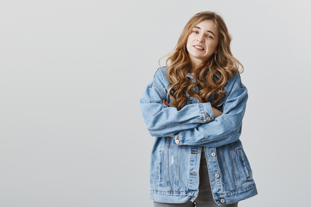 Portrait of charming emotive caucasian woman in denim jacket standing with crossed hands over gray background, showing disgust and dislike, feeling uncomfortableの写真素材