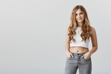 Portrait of charming sexy woman with blond hair and curly standing in cropped top, holding hands in...