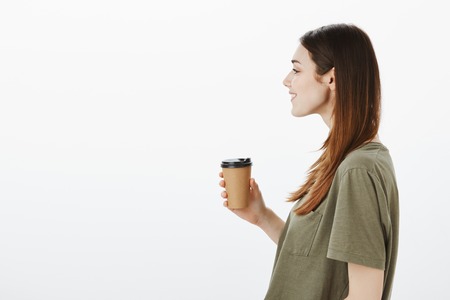 Profile studio portrait of young attractive modern girlfriend with broad smile, holding cup of...
