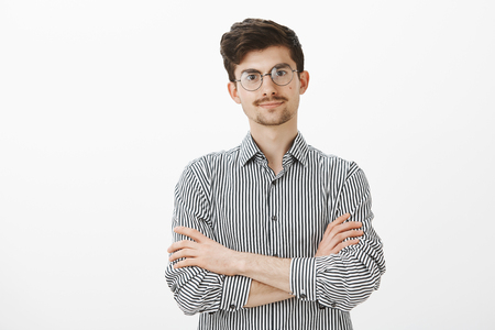 Indoor shot of displeased intense european man with beard and moustache in trendy glasses, holding hands crossed on chest and looking with await, being offended and wanting hear apologyの写真素材