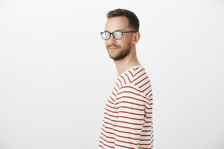 Profile portrait of friendly confident bright guy in striped pullover, turning at camera and smiling broadly, feeling relaxed and comfortable while standing against gray background casuallyの写真素材