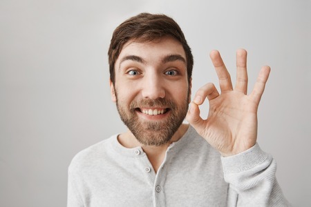 Close-up portrait of funny european guy showing okay or fine sign while smiling with excitement,...