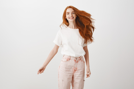 Portrait of carefree happy and charming female with ginger hair, jumping joyfully over gray background, smiling at camera, having fun and being amused, expressing joy and happinessの写真素材