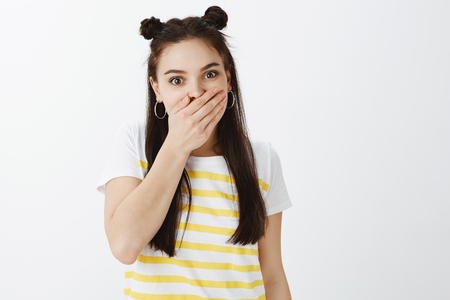 Portrait of shocked and intrigued good-looking urban woman in trendy yellow t-shirt, covering mouth with palm and staring surprised at camera, being amazed with gossip or rumorの写真素材