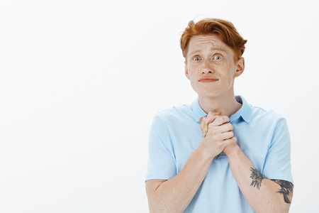 Impatient intense attractive redhead male sibling with freckles, holding hands together over chest and gazing with questioned expression at camera, begging for favour or helpの写真素材