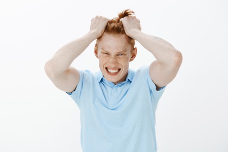 Waist-up shot of pressured depressed handsome redhead man with freckles, pulling hair out and grimacing, being pissed off and devestated, loosing lots of money and having no idea what to do nextの写真素材