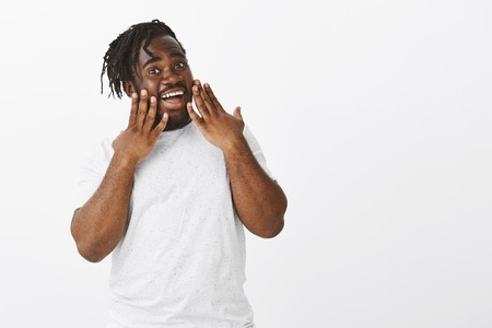 No way, awesome man. Portrait of amazed good-looking fat guy with dark-skin, holding palms on cheeks, gasping and dropping jaw from excitement and surprise, standing stunned over gray backgroundの写真素材