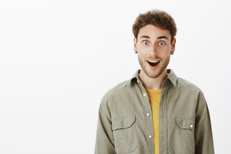 Portrait of impressed and thrilled handsome unshaven man in casual outfit, gasping and smiling, being amused and pleased with incredible great newsの写真素材