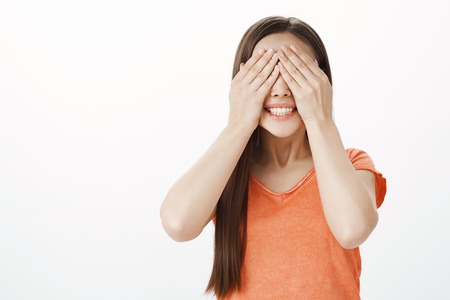 Can I open eyes already. Portrait of positive impatient european female coworker, closing eyes and covering vision with palms, smiling broadly, waiting for surprise or gift, having birthday partyの写真素材