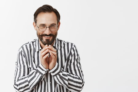 Excellent, everything goes by plan. Portrait of pleased grinning tricky man with beard and moustache having some intention in mind, steeping fingers and smiling with curious and mysterious expressionの写真素材
