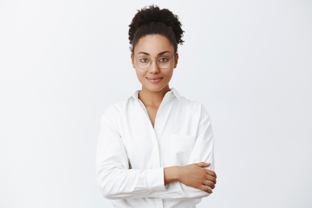 Charming friendly-looking african-american woman in glasses and white shirt, holding hands crossed on chest. smiling politely, listening customer, waiting for change in restaurantの写真素材