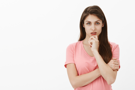 Girl stuck in tough situation, thinking how to solve problem. Portrait of focused intense smart and beautiful woman in pink t-shirt, holding arm crossed and touching chin while gazing strict at cameraの写真素材