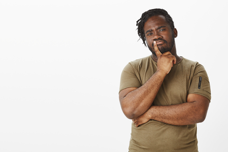Guy making importrant decision. Portrait of smart thoughtful african boyfriend in military t-shirt, frowning and holding finger on lip while thinking, making choice or being doubtful in somethingの写真素材