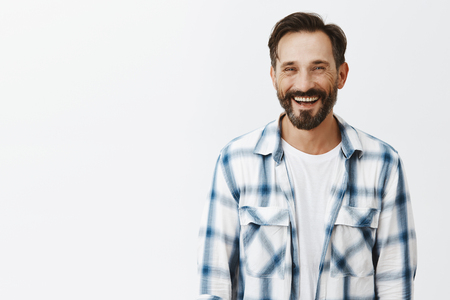Good-looking happy and friendly man with beard casually talking and laughing with coworker during lunch, standing carefree over gray background, having fun and being amused with interesting storiesの写真素材