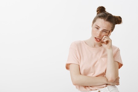 Funny caucasian girl with buns hairstyle leaning head on finger, being bored, feeling sick and tired of annoying talks, sticking out tongue in dislike, expressing boredom and careless emotionsの写真素材
