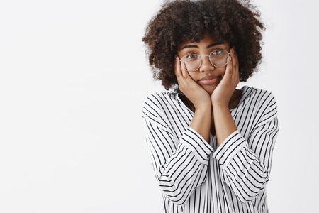 Waist-up shot of tired and gloomy indifferent dark-skinng young girl with afro hairstyle squeezing...