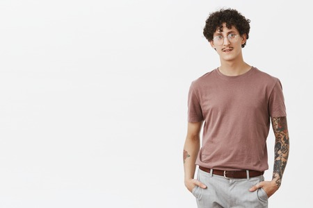 Stylish modern young man with fancy moustache, curly dark hair and tattoos on arms holding hands in...