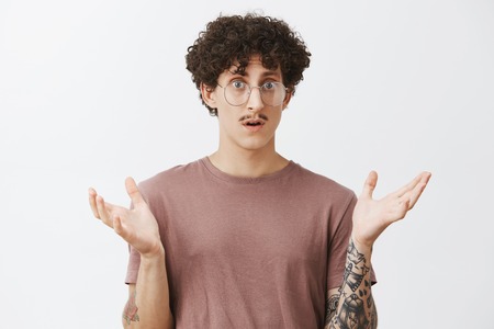 Man in stupor feeling confused cannot understand what happened standing with raised aside palm and opened mouth gazing clueless and shocked at camera feeling frustrated over gray backgroundの写真素材