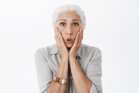 Waist-up shot of amazed and surprised emotive senior lady with grey hai folding lips in wow sound...