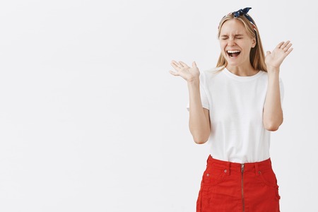 Studio shot of silly overemotive attractive and stylish girl with carefree and happy excpression waving palms near face and laughign out loud with closed eyes being very surprised and joyfulの写真素材