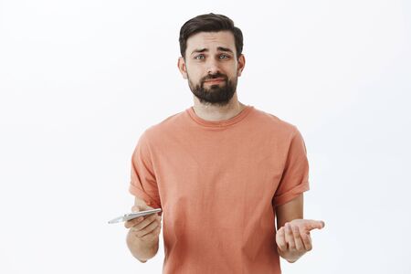 Unimpressed and displeased guy holding smartphone feeling displeased after using new device thinking...