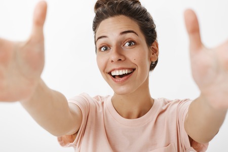 Headshot of sincere happy and friendly attractive caucasian female pulling hands towards camera to grab or give warm sweet hug smiling joyfully wanting cuddle with friendの写真素材