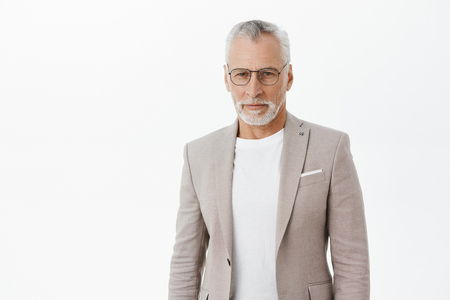 Self-assured smart and intelligent senior rich businessman in glasses an elegant suit standing confident and looking at camera focused and determined ready accomplish anything over grey wallの写真素材