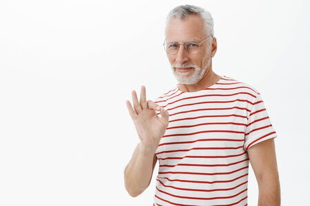 Old charismatic and self-assured man staying chill and cool showing okay gesture and smiling...