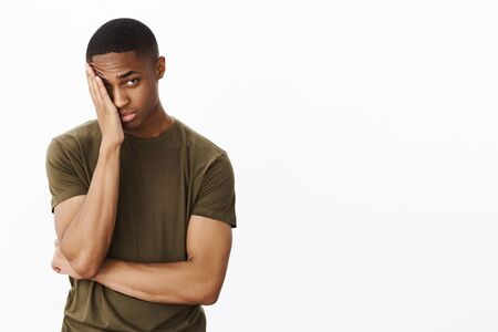 Portrait of man feeling embarrassed making facepalm gesture putting hand to half of face peeking at camera with tired blushing expression standing displeased and exhausted over gray backgroundの写真素材