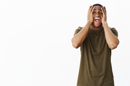 Guy feeling sad yelling out loud squeezing head with hands on face making miserable expressing feeling fed up, distressed and troubled, losing control over emotions after heartbreaking break-upの写真素材