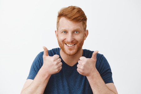 Supportive and attractive adult redhead male with bristle liking great plan raising hands, showing thumbs up, smiling joyfully, accepting nice idea or cheering friend who trying talk to charming womanの写真素材