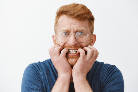Guy freaking out, feeling worried and scared someone know his secret, biting fingernails and frowning staring intense at camera, having terrible thoughts in mind, overreacting and panickingの写真素材