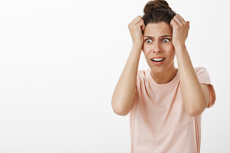 Girl freaking out starting panic as realising she pregnant feeling worried and anxious holding hands on head frowning and grimacing intense looking down with bothered confused expressionの写真素材