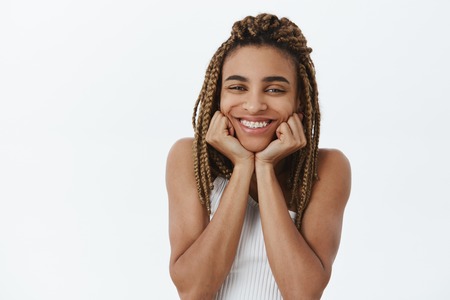 Indoor shot of carefree delighted dark-skinned girlfriend with dreadlocks and braces smiling...