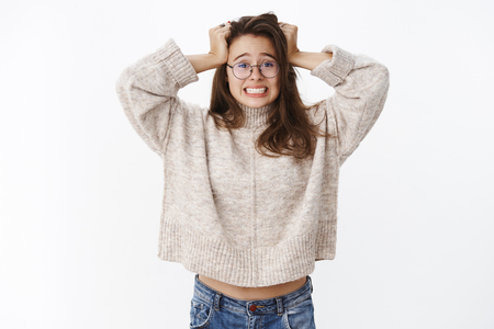 Jeez I am in trouble. Portrait of worried and freaked out young girl clenching teeth and holding hands on head in despair, feeling nervous and anxious as having troublesome situationの写真素材