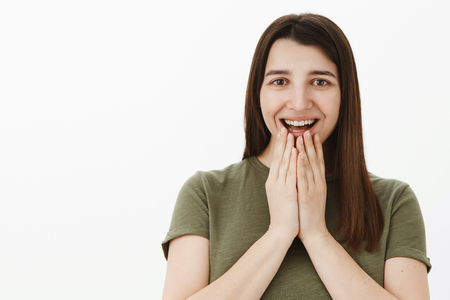 Amazed happy woman pleased received awesome gift did not expect that comming holding hands on lower lip smiling delighted as anticipating awesome present over gray backgroundの写真素材
