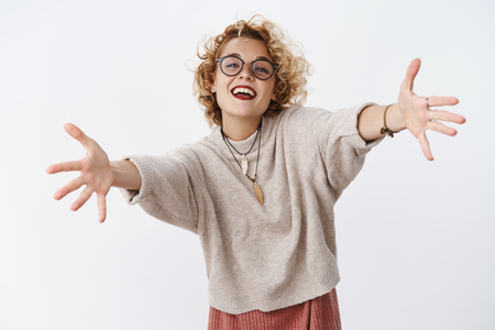 Girl wants hugs. Portrait of charming happy and enthusiastic attractive european female with short blond hair in glasses and sweater stretch hands to camera for cuddles and smiling friendly, welcomingの写真素材