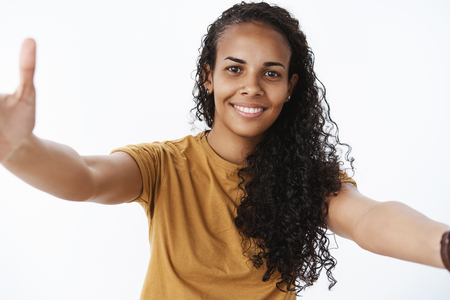 Portrait of friendly optimistic and joyful african-american woman with long curly hair pulling hands forward to cuddle and comfort upset friend over gray backgroundの写真素材