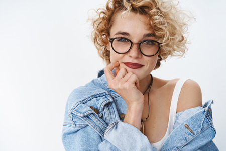 I got excellent idea. Portrait of creative and confident good-looking european female blogger in glasses and denim jacket holding hand on cheek and chin smirking delighted, having plan thinkingの写真素材