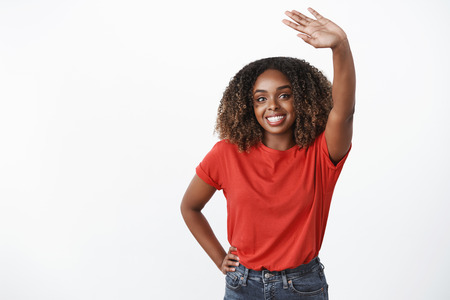Bye see you later, take care. Portrait of friendly and sincere kind gentle african-american woman waving raised palm in greeting or goodbye gesture smiling holding hand on waist over white backgroundの写真素材