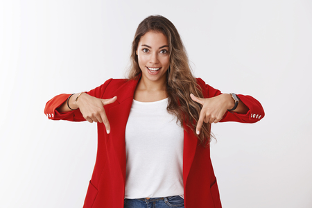 Girl suggest look downward great promotion raise company income. Excited good-looking assertive young female entrepreneur wearing red jacket pointing down smiling ambitious, white backgroundの写真素材