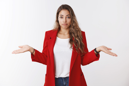 Unaware clueless cute shrugging caucasian curly-haired girl holding hands sidewards pursing lips uncertain perplexed find answer having no idea, not know, unfamiliar topic, standing white backgroundの写真素材