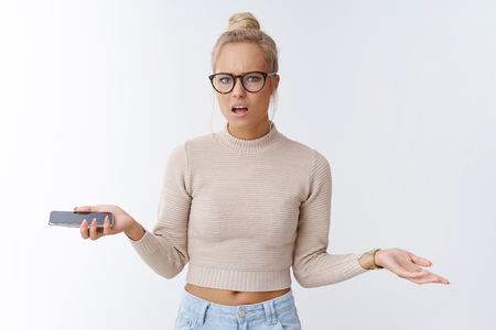What your problem. Portrait of irritated pissed and freaked out bothered bossy blond businesswoman in glasses spread hands in dismay holding smartphone complaining frowning over white backgroundの写真素材