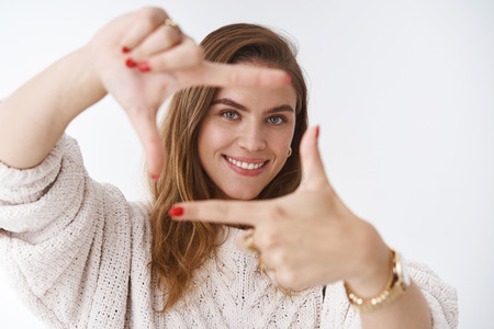 Creative good-looking woman using imagination picturing new appartment design how capture you making finger frame looking through curious delighted standing amused happy, smiling white backgroundの写真素材
