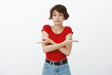 Silly awkward confused attractive woman short haircut cross arms pointing sideways left right biting lip uncertain stare camera worried cannot make choice not sure what decision offer bestの写真素材