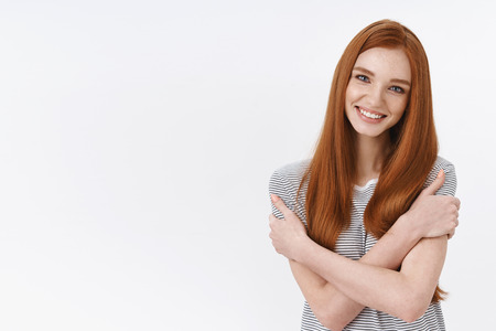 Charming european redhead feminine young girl hugging herself hold shoulders tilting head smiling flirty romantic attitude, standing delighted white backgroundの写真素材