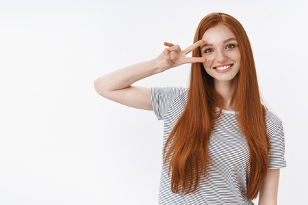 Positive cute optimistic redhead teenage girl have fun showing peace victory gesture hold disco sign eye tilting head smiling broadly enjoy having fun cool party, standing white backgroundの写真素材