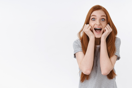 Lively amused thrilled happy young cute redhead girl popping blue eyes surprised screaming cheerfully excited see favorite popular singer standing white background amazed, attend awesome concertの写真素材