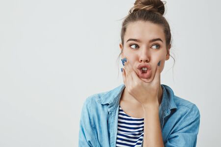 Studio shot funny charismatic european attractive young woman brunette hairbun, looking aside squeez cheeks mouth, folding lips showing front teeth mimicking bunny, feeling silly carefreeの写真素材
