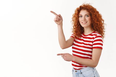 Can you help me get it. Happy good-looking redhead curly feminine woman striped t-shirt pointing left index fingers look camera entertained smiling asking advice making choice, picking products storeの写真素材
